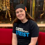 MacKenzie Morgan Bonasena, bestyrelsesmedlem i Ateistisk Selskab Smilende ung person iført t-shirt med påskriften filmnørd, cand.scient.soc, ateist. Siddende i den røde sofa hos Go'Aften Danmark