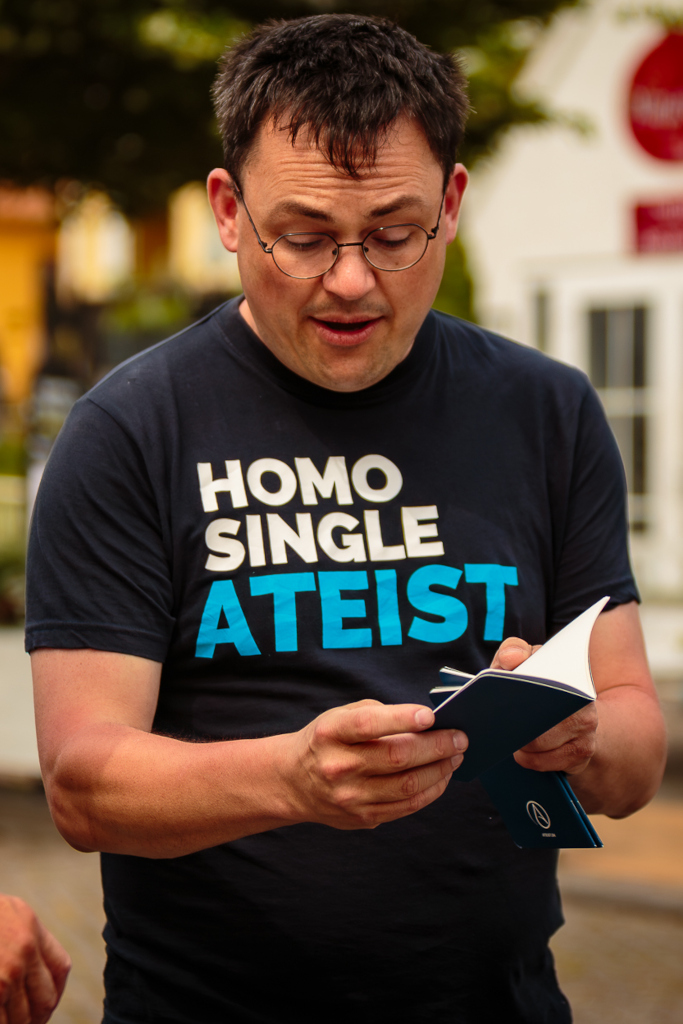 Medlem af Ateistisk Selskab, Rasmus Malver, på Folkemødet 2025 iført ATEIST t-shirt med teksten homo, single, ateist. Flot ung mand mand med mørt hår og en passioneret personlighed.