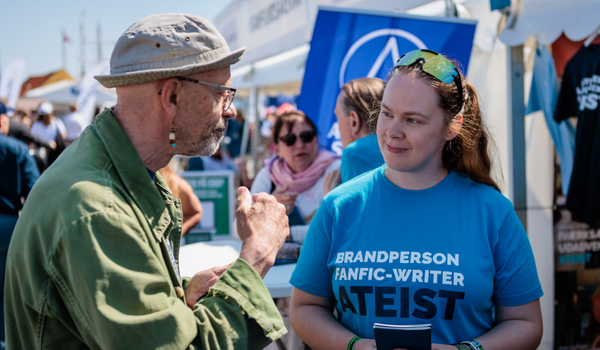 Smilende bestyrelsesmedlem Mac Morgan Bonasena, Ateistisk Selskab, i engageret samtale med gæst på Folkemøde Bornholm. På Macs t-shirt ordene brandperson, fanfic-writer og ateist.