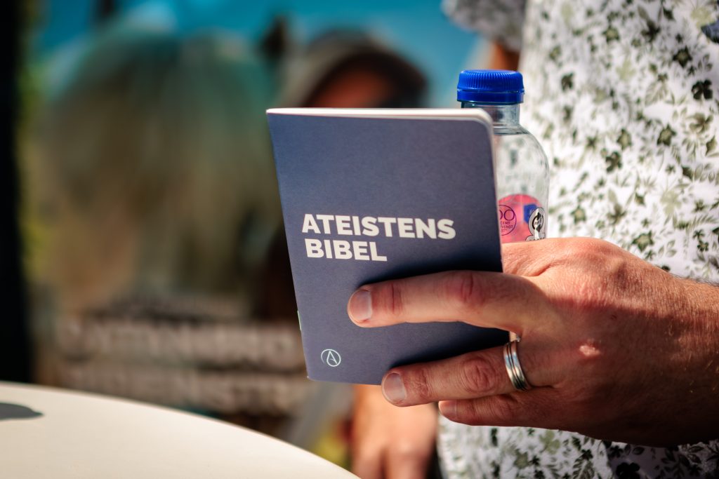 Ateistens Bibel og en flaske vand i hånden på en moden mand med vielsesring