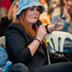 Yngre kvinde med langt rødt hår og bøllehat i dialog på Ateistisk Selskabs stand på Folkemødet 2026 på Bornholm